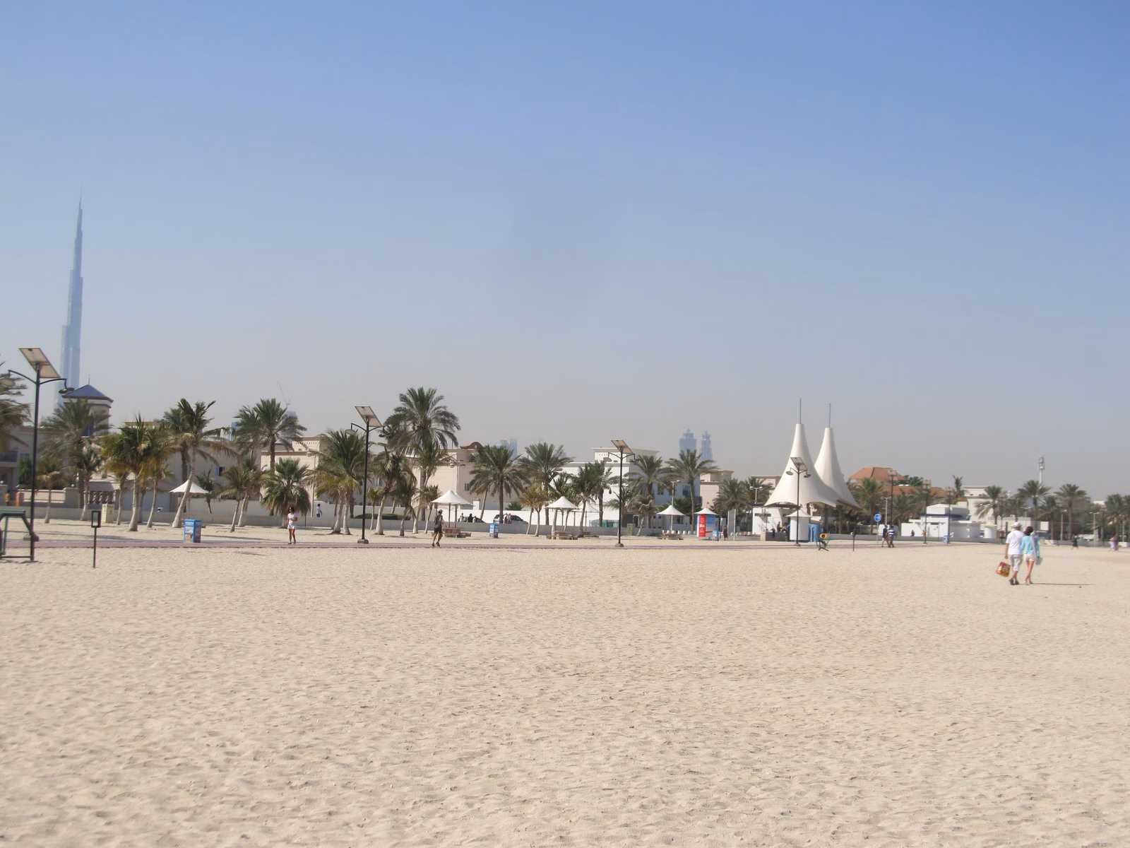 Wide sandy Jumeirah Public Beach in Dubai with palm trees and the Burj Al Arab on the horizon, one of the beaches with accessible facilities