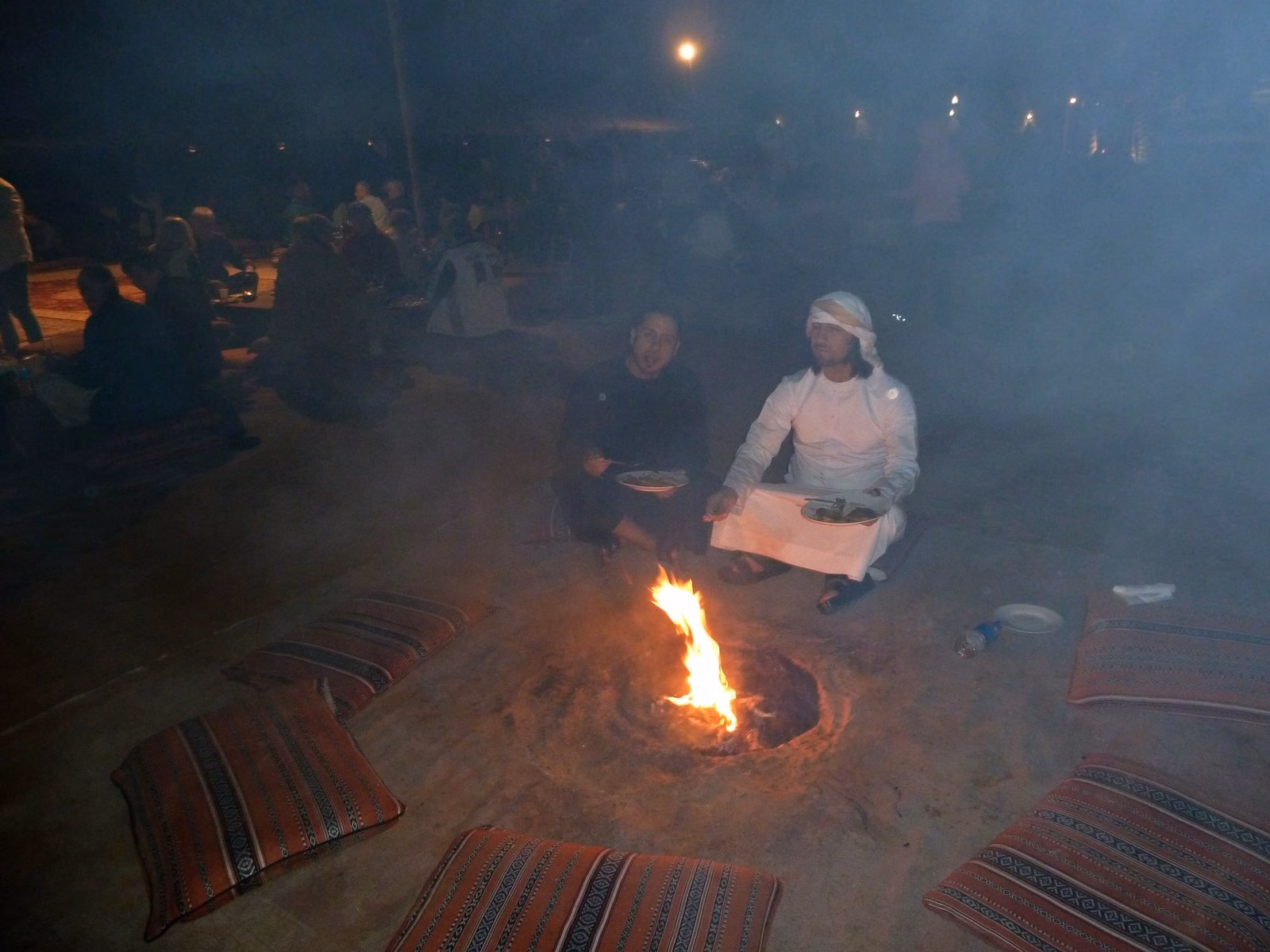 Guests seated on rugs around a campfire at a desert camp near Dubai at night, part of the Dubai winter camping tradition