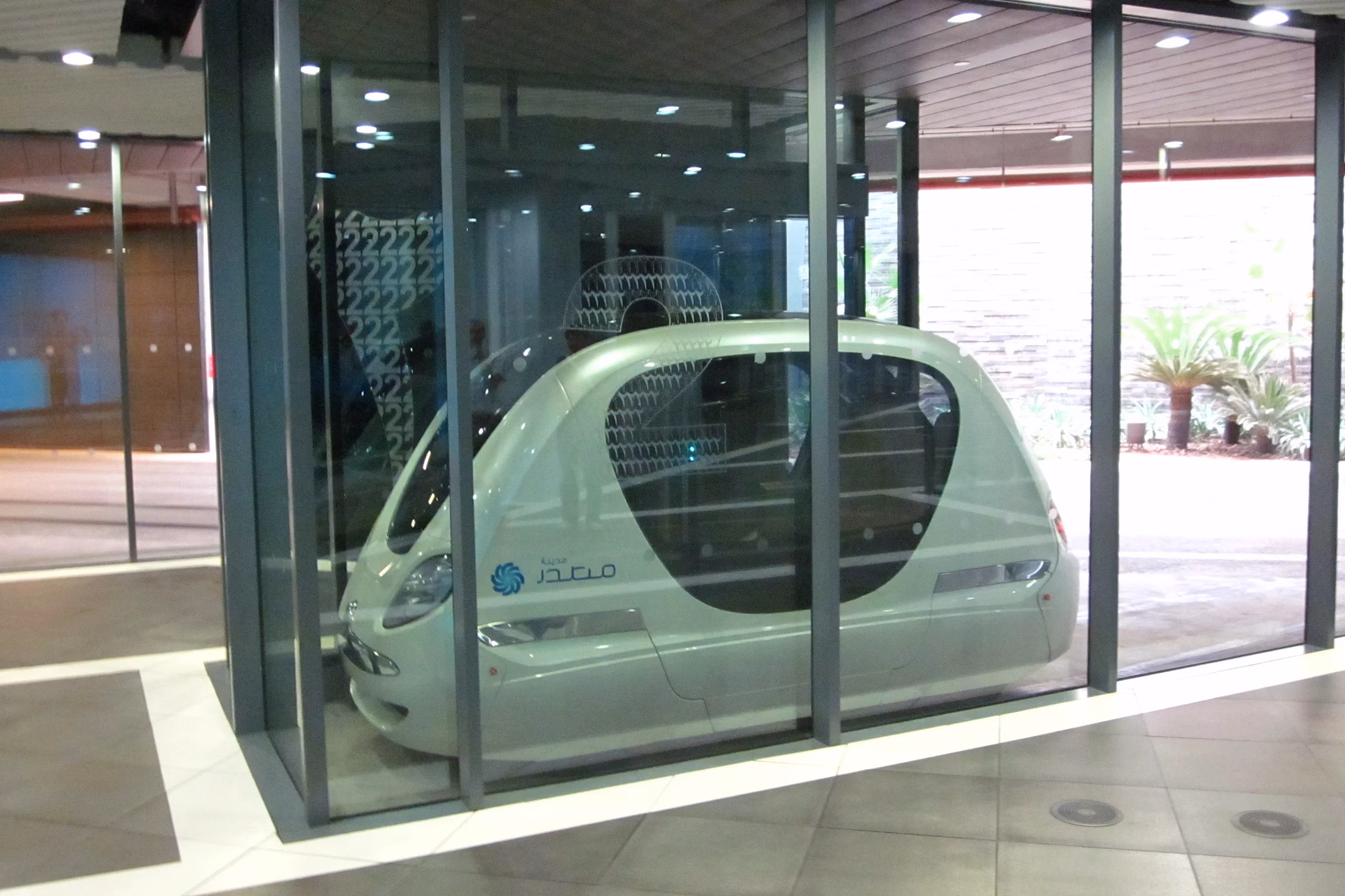 Small driverless electric podcar waiting at a glass-walled station, illustrating how Dubai driverless pods on dedicated guideways could look