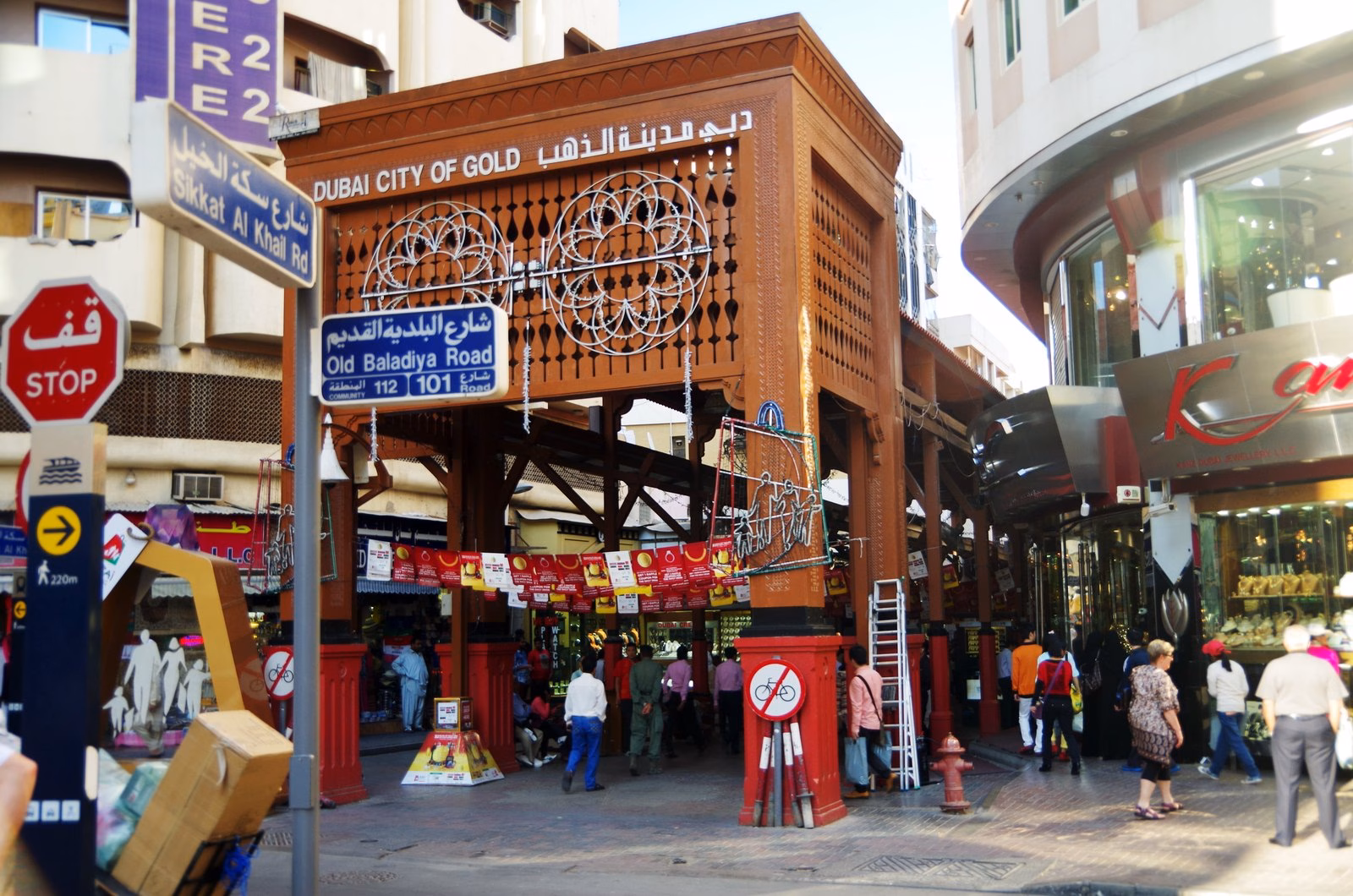 The ornate wooden entrance arch of the Dubai Gold Souk in Deira, with shoppers walking beneath it