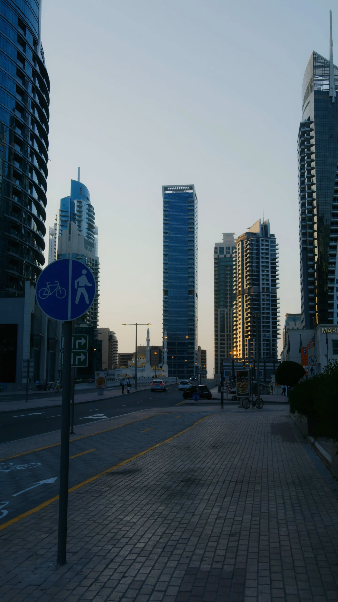Blue shared cycling and walking path sign on a quiet Dubai street lined with towers at dusk