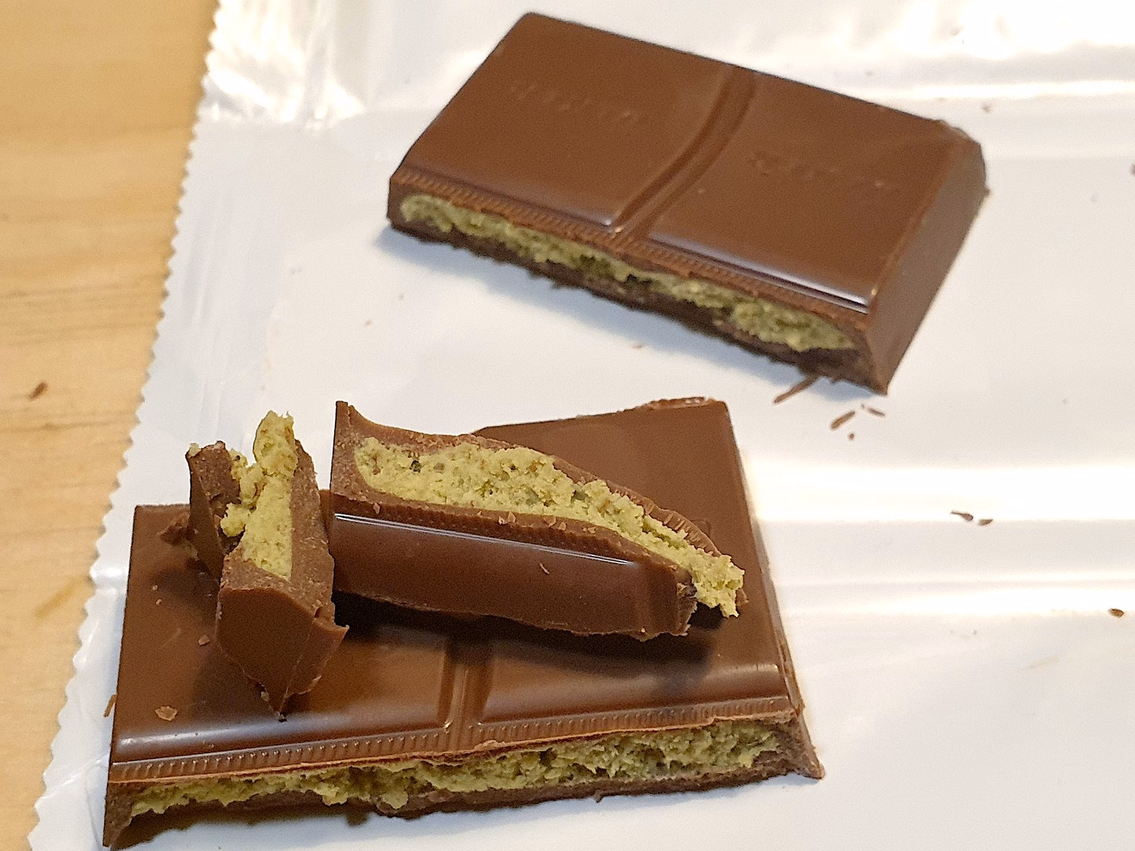 A Dubai-style chocolate bar cut into pieces on its wrapper, showing the thick pistachio cream filling