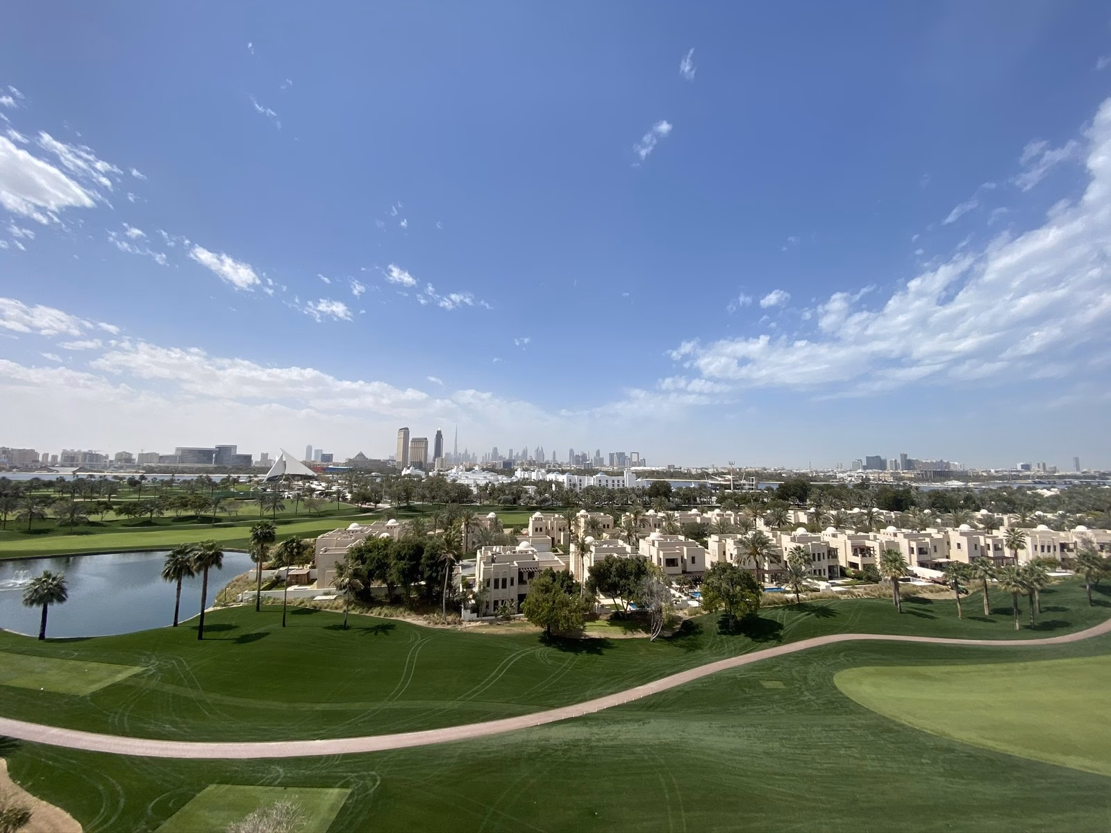 A green fairway curving past lakeside villas under a blue sky, one of the many places to play golf in Dubai