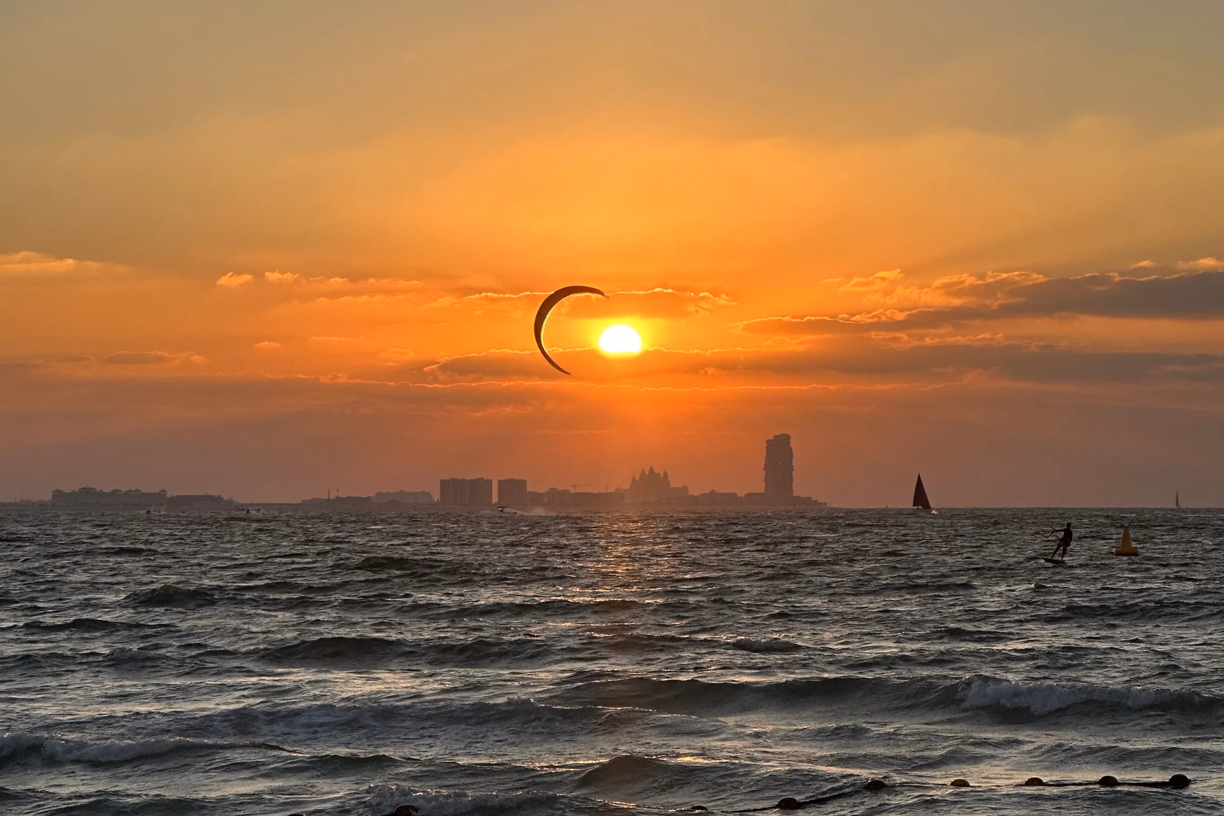 A kitesurfer riding the waves off Kite Beach in Dubai at sunset, with the kite silhouetted against the sun