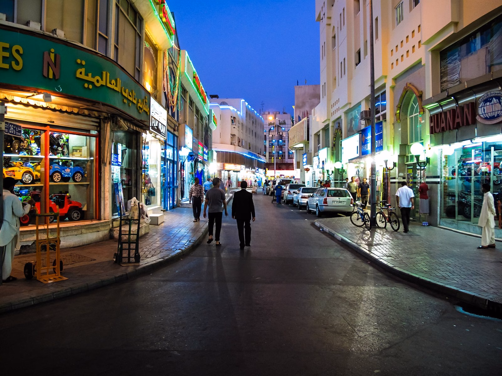 Shoppers walking along a lit shopping street in old Deira, Dubai, in the early evening