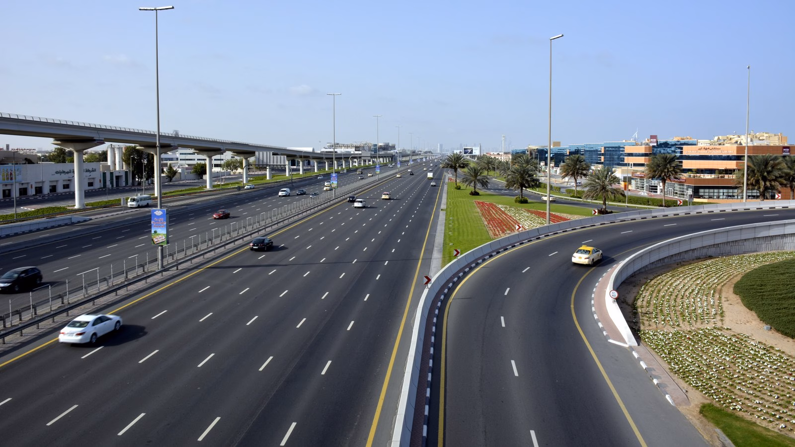 A quiet, wide Sheikh Zayed Road beside the Dubai Metro viaduct early on a Friday morning, a reminder to drive to the posted limit even on empty roads
