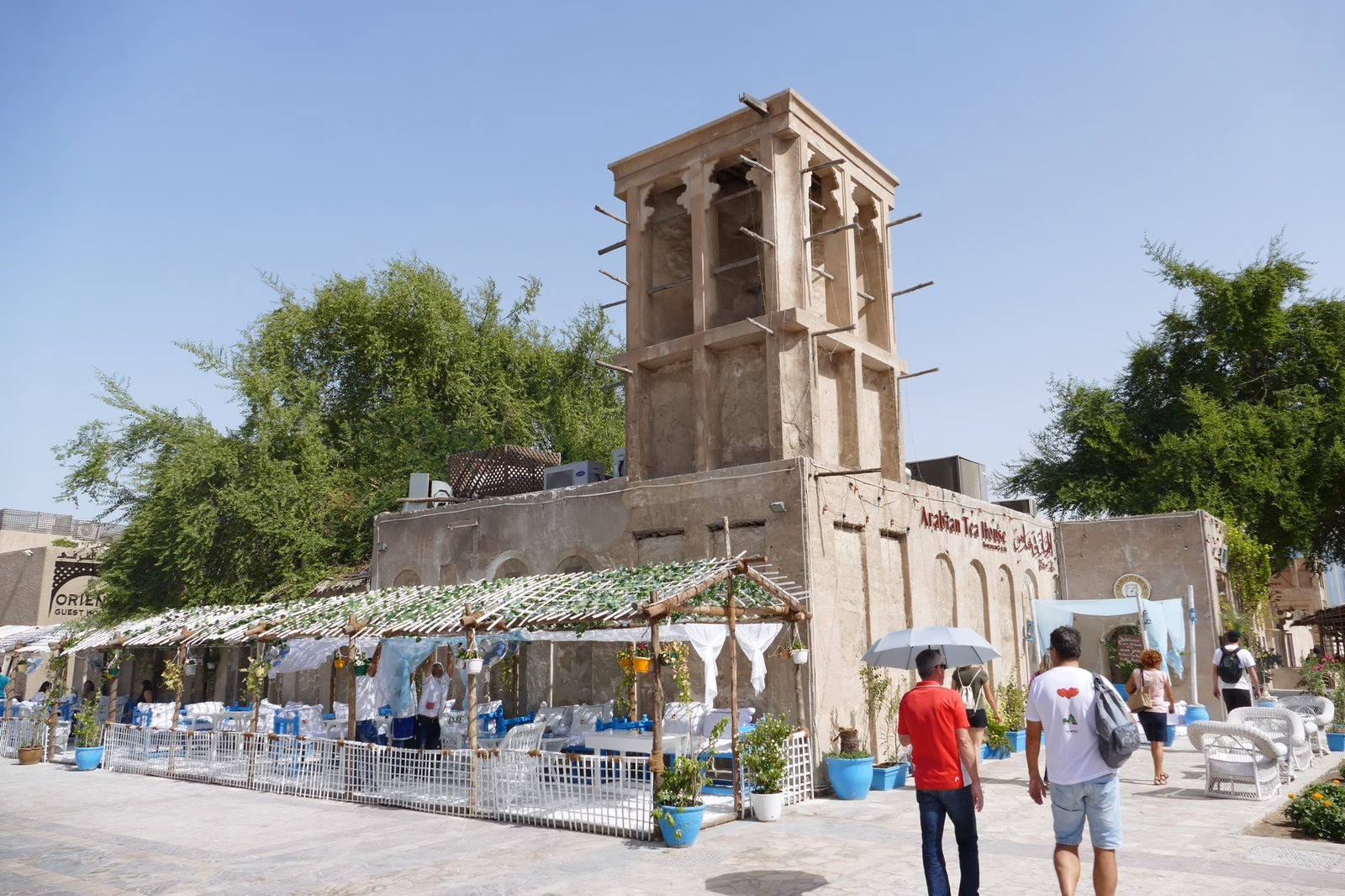 Visitors walking past a wind tower and a shaded café in Al Fahidi Historical Neighbourhood, Bur Dubai