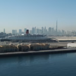 The QE2 moored at Port Rashid with the Dubai skyline and Burj Khalifa behind, beside the waterfront peninsula of Dubai Maritime City